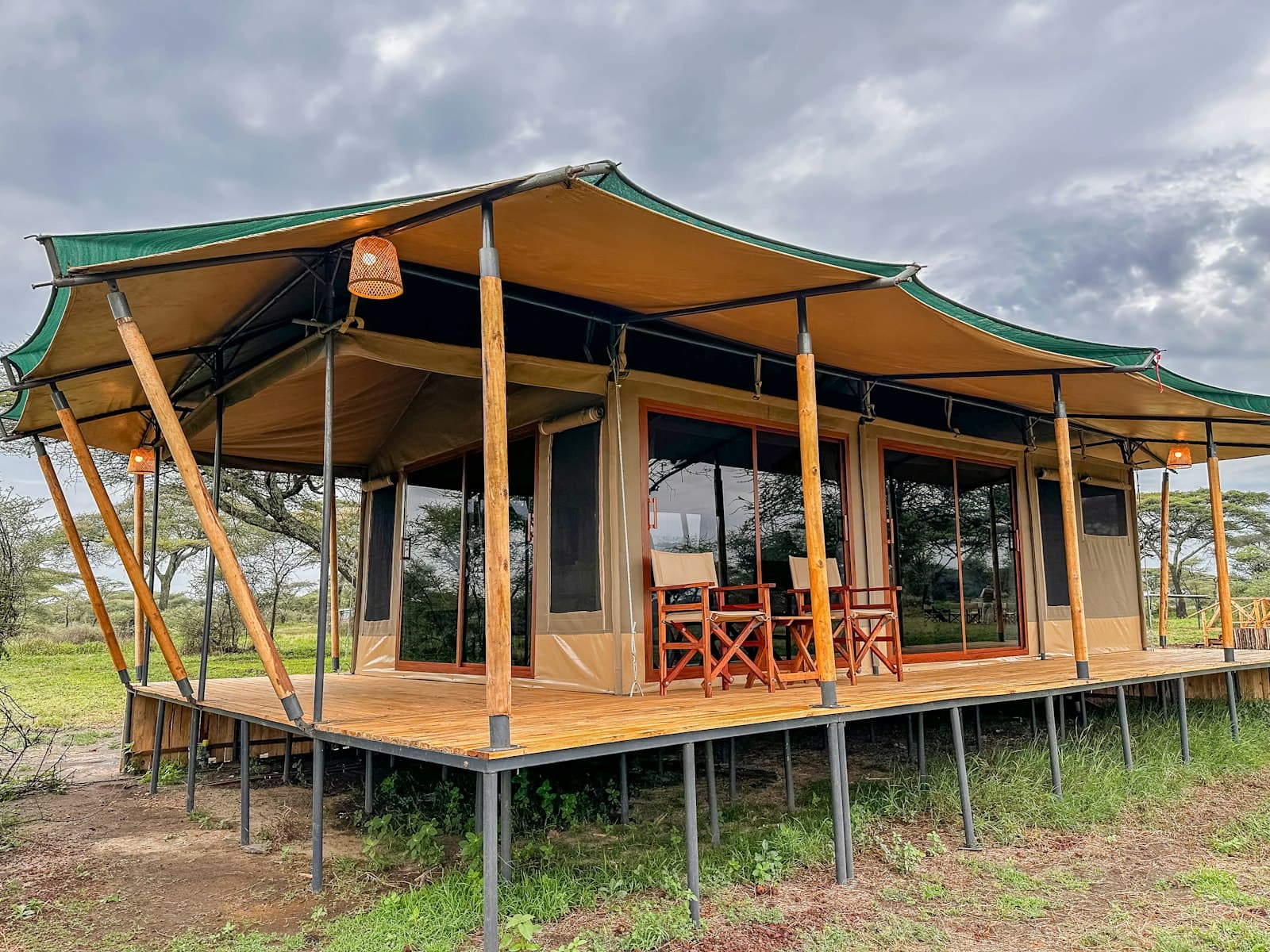 A luxury safari lodge tent on a raised wooden deck among acacia trees