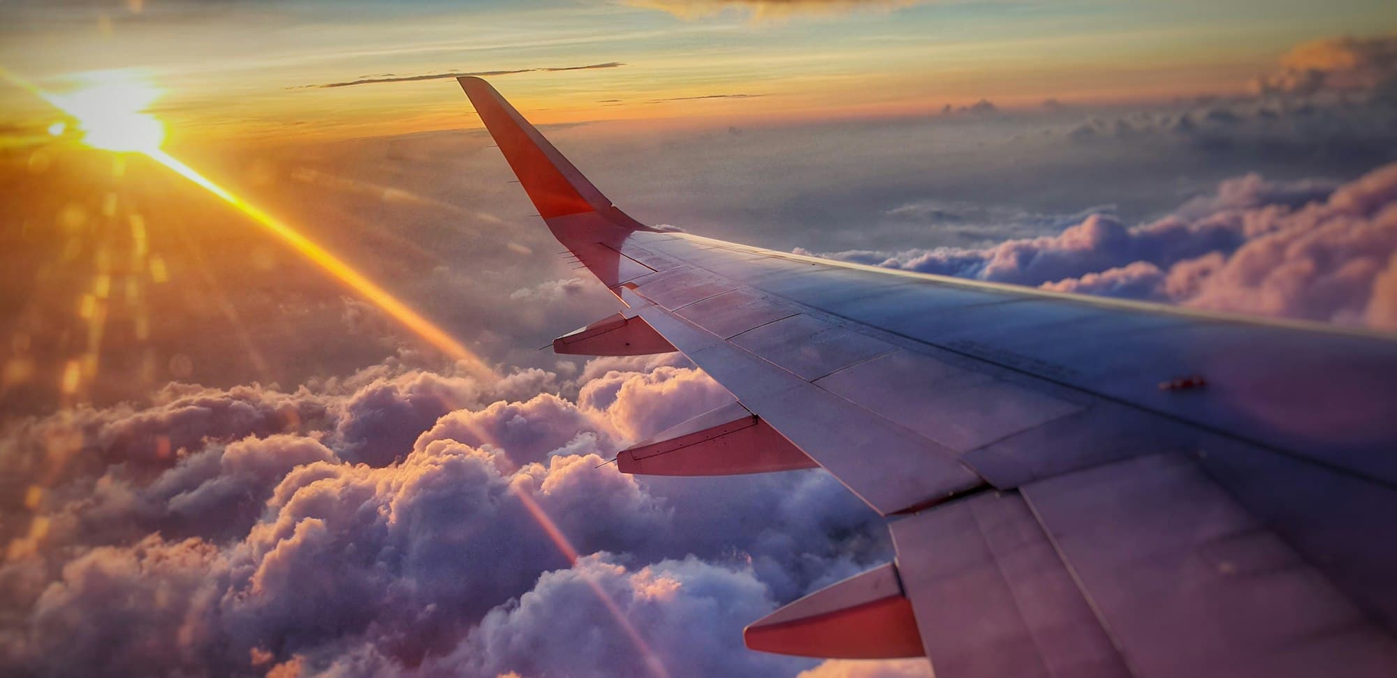 An airplane wing over sunset clouds — destination to be determined