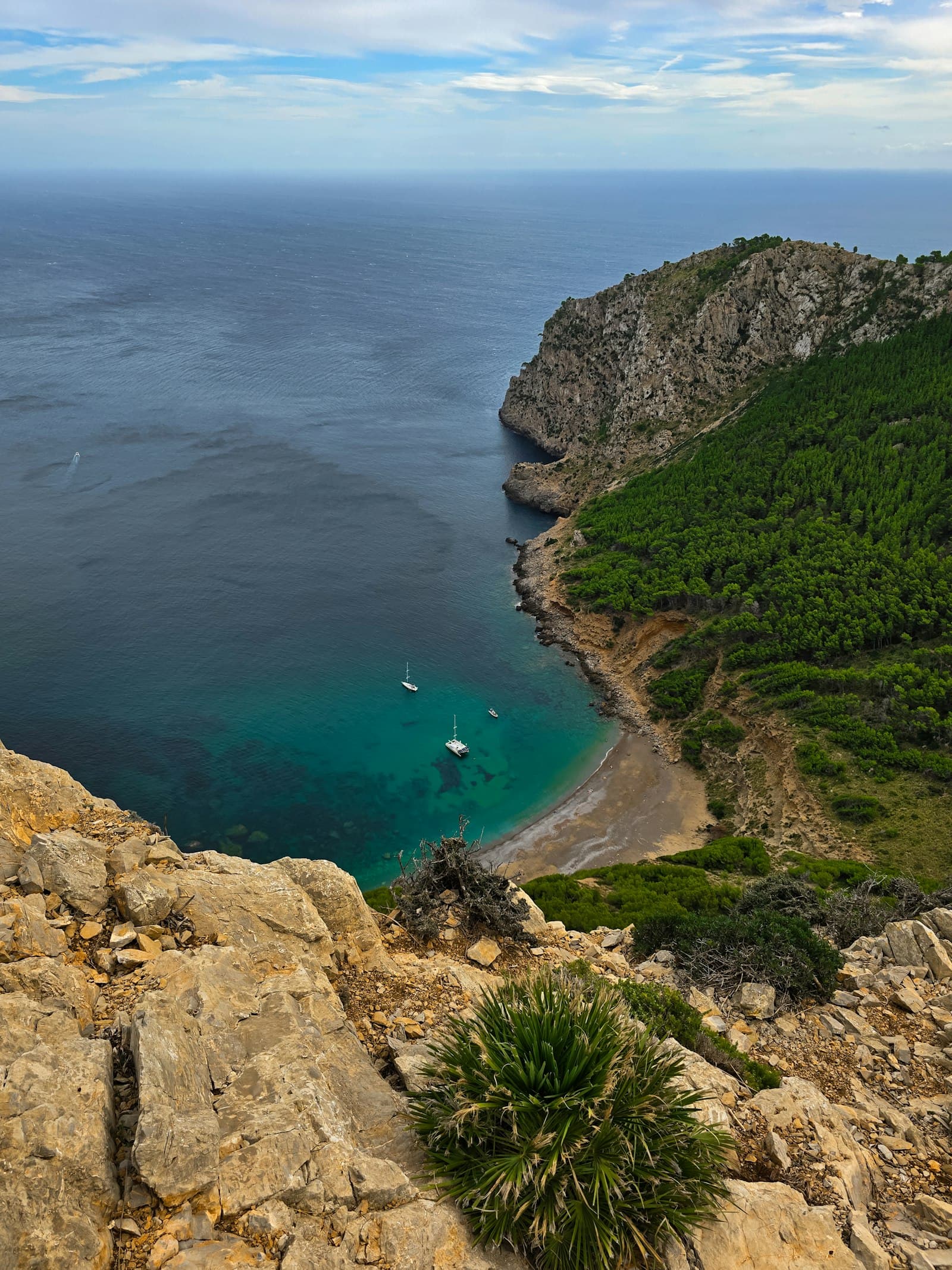A turquoise Mallorcan cove with sailboats at anchor, seen from the cliffs